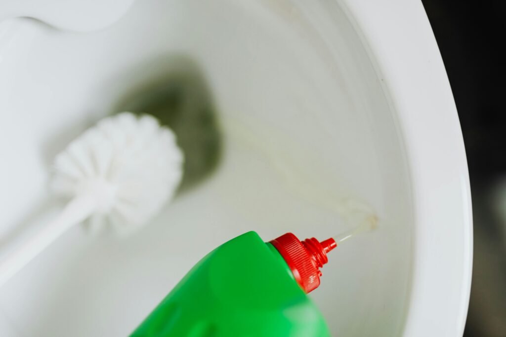 Person cleaning a toilet with a brush and disinfectant, focusing on removing stains and grime.