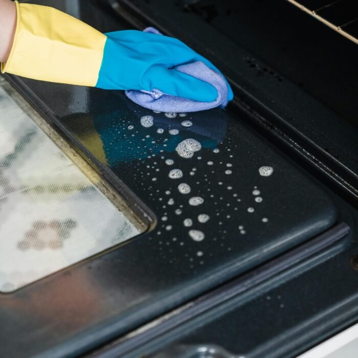 Person cleaning the inside of an oven, scrubbing away grease and burnt food for a spotless finish.