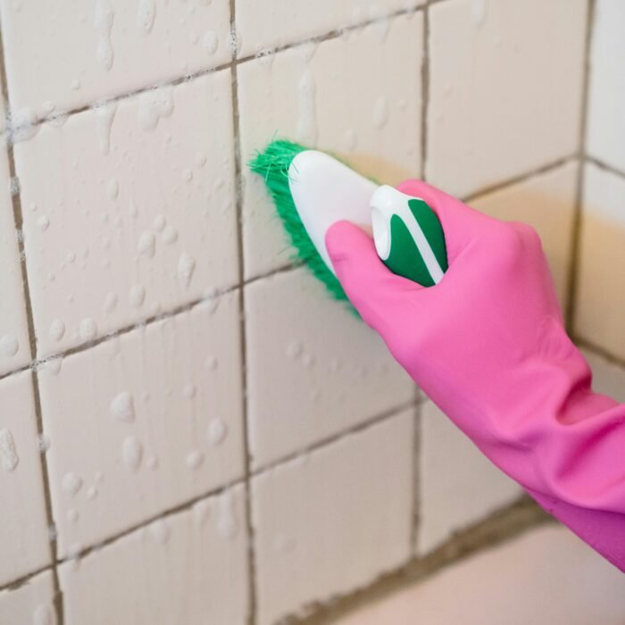 Person scrubbing grout lines with a cleaning brush to remove dirt and stains for a spotless finish.